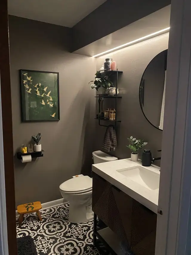 Gray bathroom with white vanity top, round mirror and open shelving over the toilet