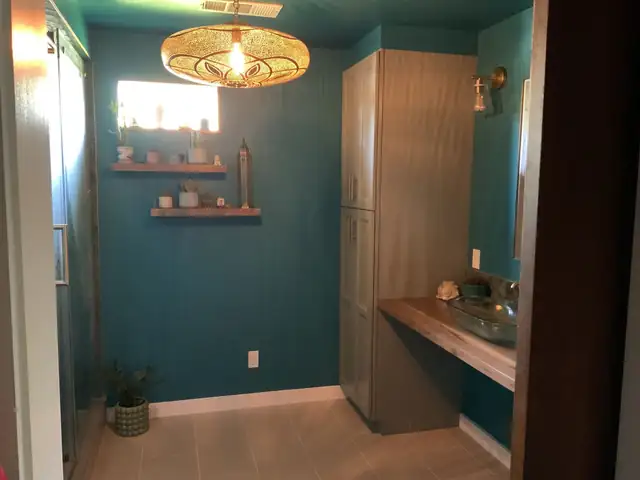 Teal bathroom with built-in wood vanity counter, vessel sink, tall linen cabinet and woven pendant light
