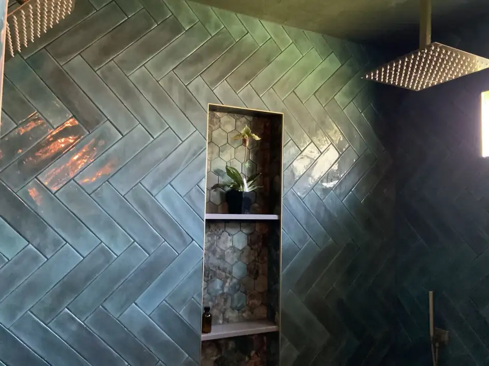 Glossy green herringbone tile shower with a tall tiled niche and square rain shower head, from bathroom remodeling in Lafayette, LA by Very Good Carpentry