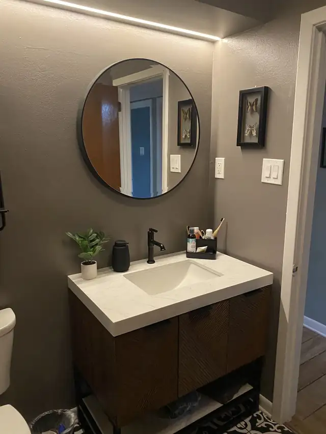 Floating dark wood vanity with a white integrated sink, black faucet and round black mirror on a gray wall
