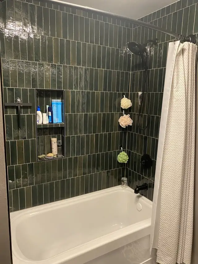 Tub surround in dark green vertical tile running to the ceiling, with a recessed shampoo niche